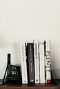 Collection of different books and cup for tea with saucers placed on wooden shelf against white wall