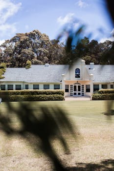 Colonial style building surrounded by lush greenery and serene landscape under a vibrant blue sky.