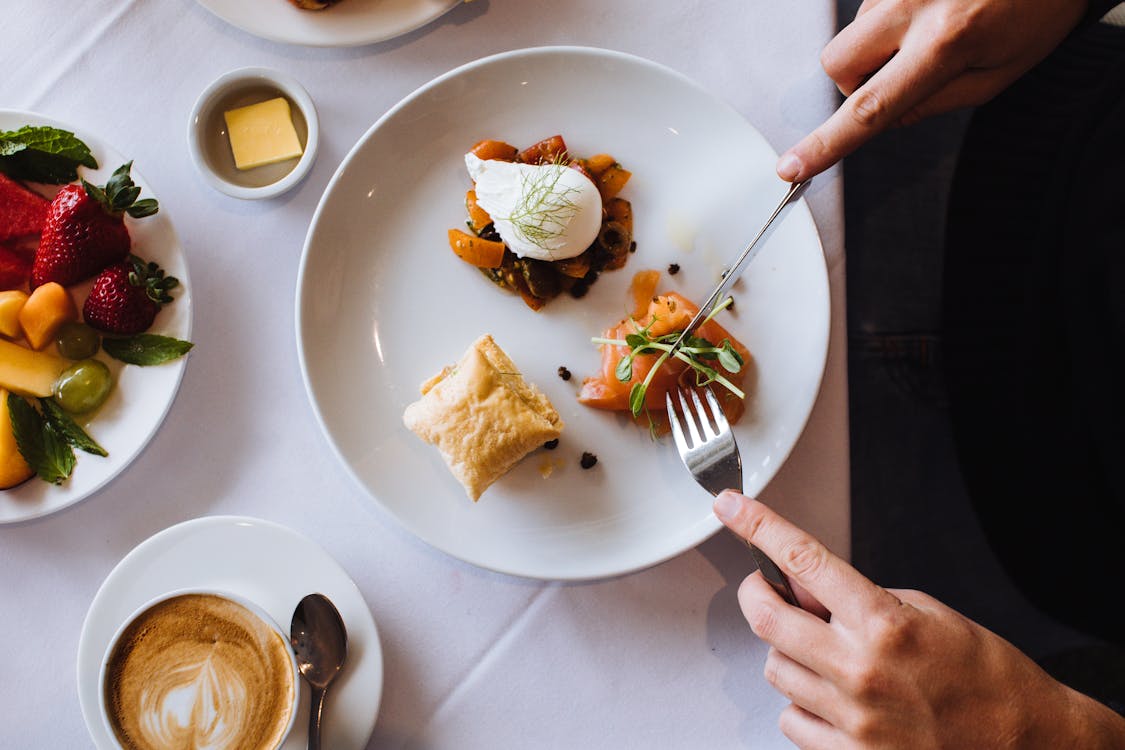 Top view of crop anonymous person having tasty appetizing breakfast with fork and knife having hot aromatic coffee