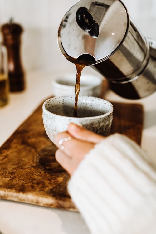 Free Crop anonymous female in white sweater pouring hot aromatic coffee from metal kettle into ceramic cup Stock Photo