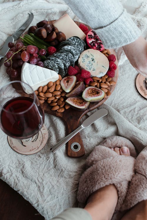Free Elegant cheese platter featuring fruit, nuts, and a glass of wine. Perfect for a cozy evening. Stock Photo