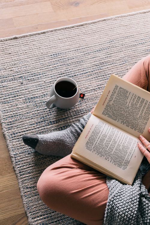 Free Overhead view of a person reading a book on a cozy carpet with a cup of tea. Stock Photo