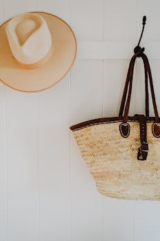 Elegant straw hat and wicker bag hanging on a clean white wall, showcasing minimalistic style.