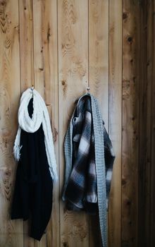 Warm coats and soft scarfs hanging on racks on wooden wall at home