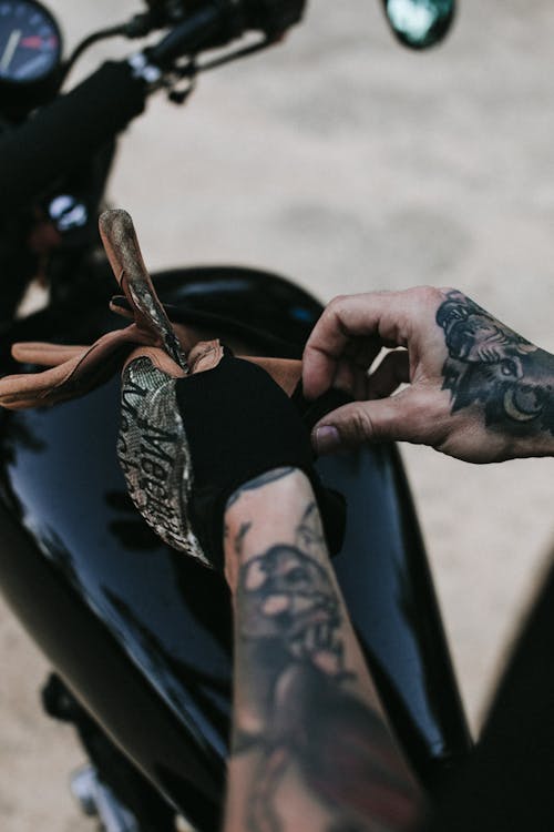 Free From above of crop unrecognizable male biker wearing leather glove on tattooed hands before riding motorcycle Stock Photo