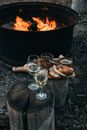 High angle of fire bowl with burning flame and glasses of white wine with snacks on wood stumps