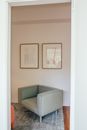 Interior of light room in house with big armchair on carpet and paintings hanging from white wall