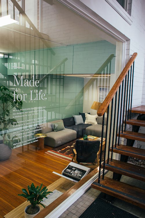 Stairway leading to modern lounge zone with glass wall and couch with pillows near table and armchair and potted plants