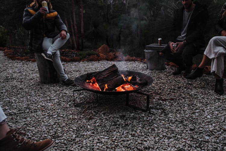 Unrecognizable Travelers Sitting Near Campfire In Woods