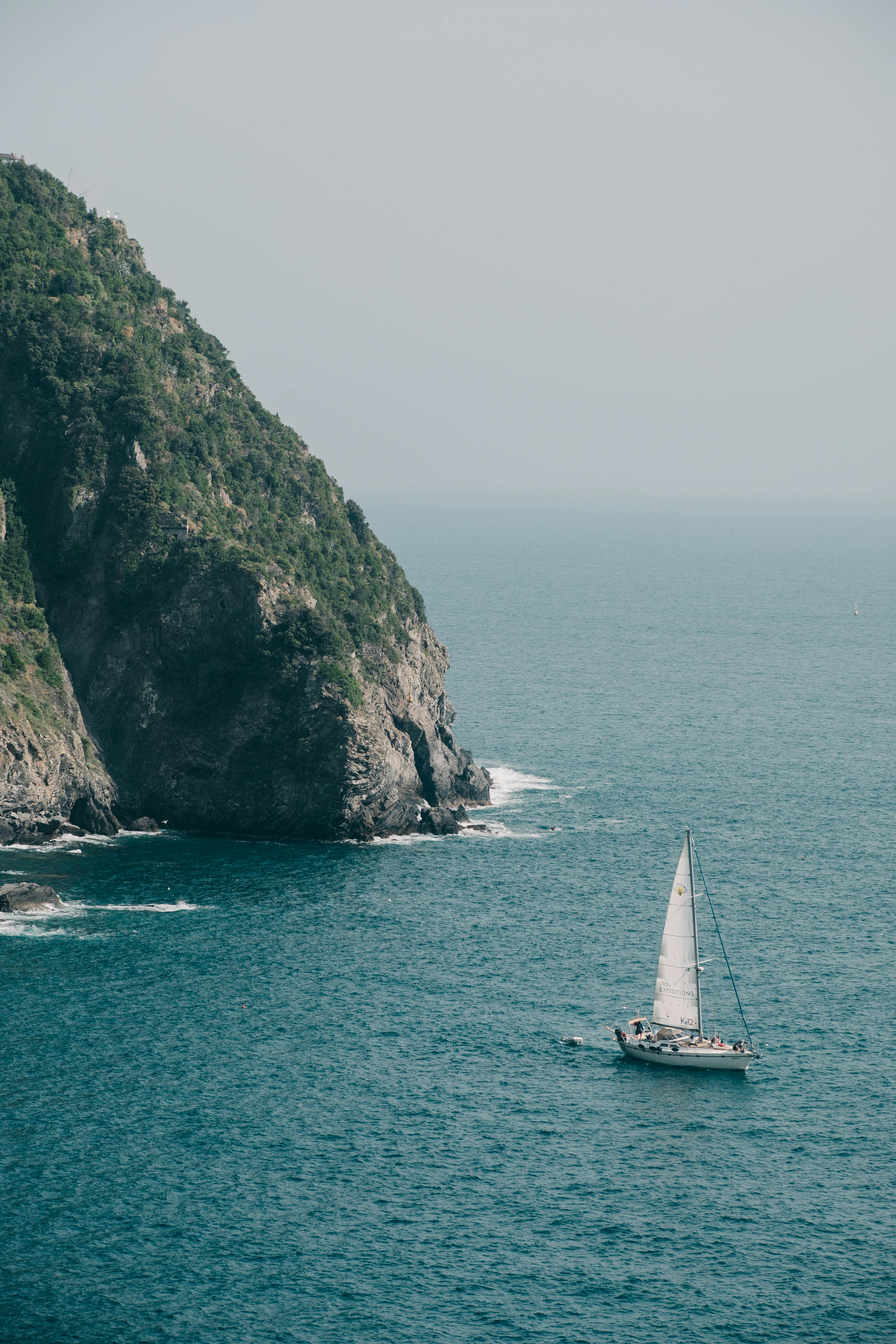 一艘帆船在明亮的天空下在岩石悬崖附近航行的宁静场景