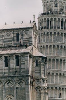 Exterior of aged stone church decorated with ornate elements and Leaning Tower of Pisa with tourists on top