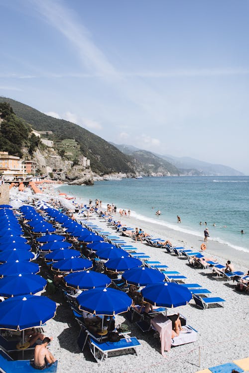 Free From above of blue parasols and sunbeds on sandy beach with people sunbathing and swimming in azure sea water Stock Photo