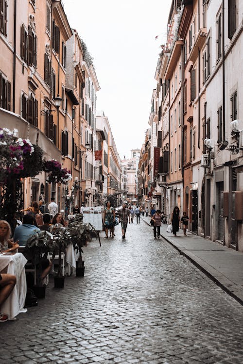 Free Narrow paved street between old residential houses with people walking along and sitting in cafe Stock Photo