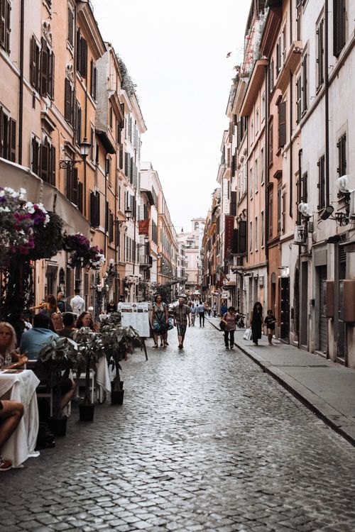 Free Narrow paved street between old residential houses with people walking along and sitting in cafe Stock Photo