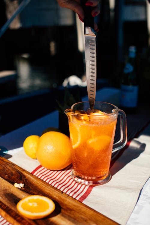 Crop woman stirring drink with orange