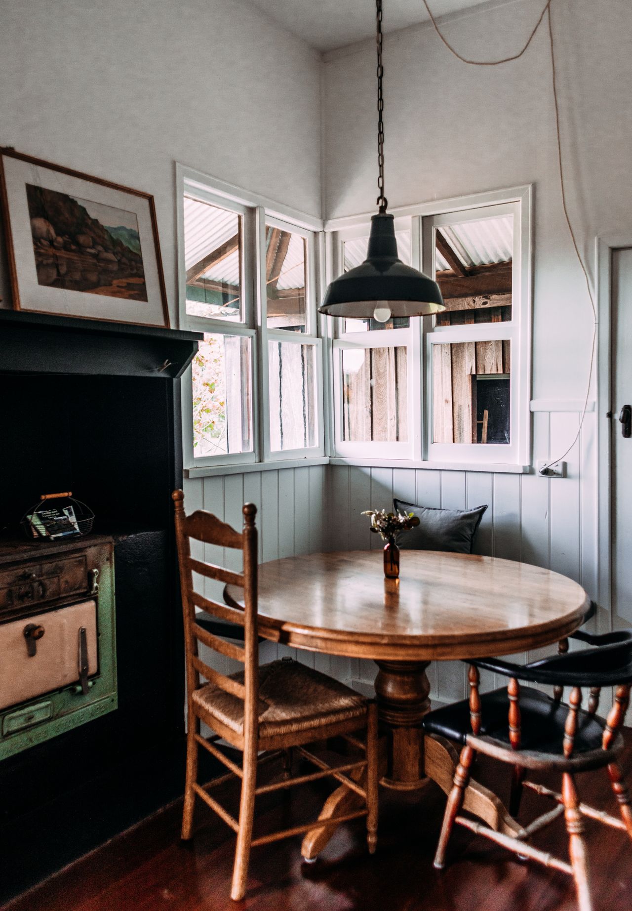 Wooden ladder-back side chair and dark wooden armchair around a round pedestal table in a farmhouse nook
