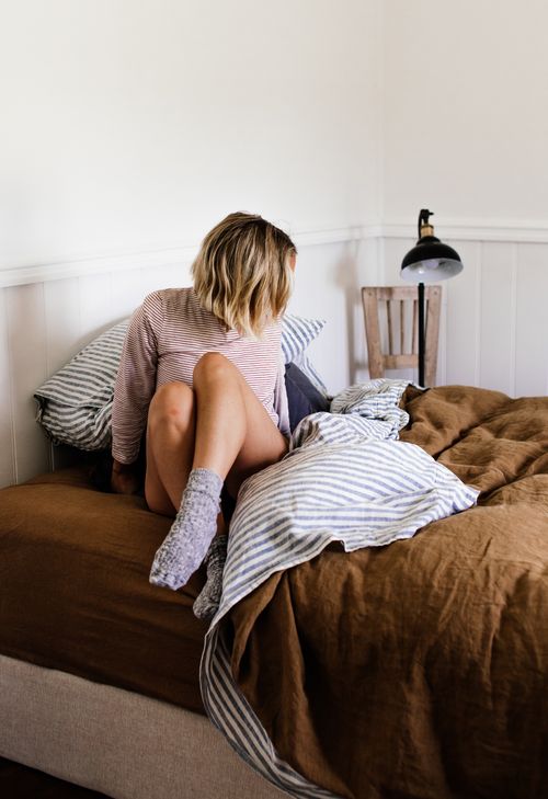 Free Anonymous blond female in home wear and socks sitting on soft bed with creased cover Stock Photo