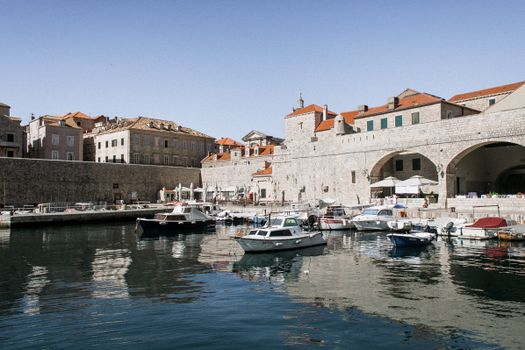Aged urban harbor with nautical transport on Adriatic Sea against building facades in Dubrovnik Croatia under blue sky
