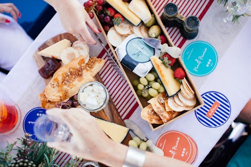 Crop girlfriends at table with assorted delicacies and fresh fruits