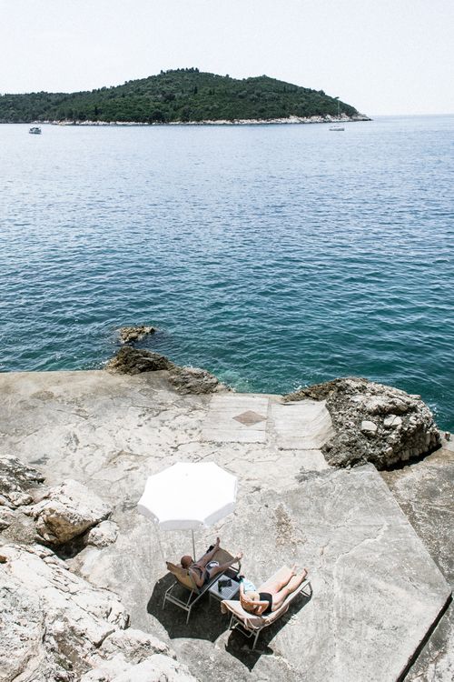 Free From above of anonymous travelers on sunbeds enjoying rippled ocean and mount during trip on sunny day Stock Photo