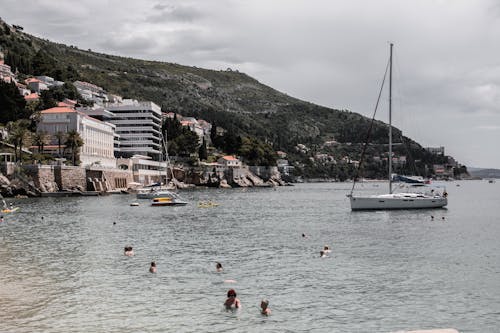 Unrecognizable travelers swimming in sea against houses on mount