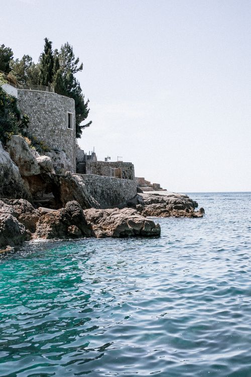 Free Aged stone construction facade on mount with trees against rippled sea under light sky in summer Stock Photo