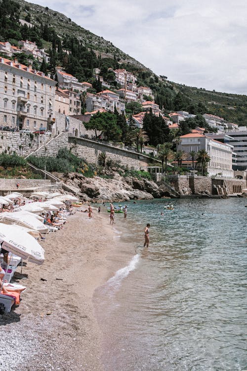 Anonymous travelers on sea beach against houses on ridge