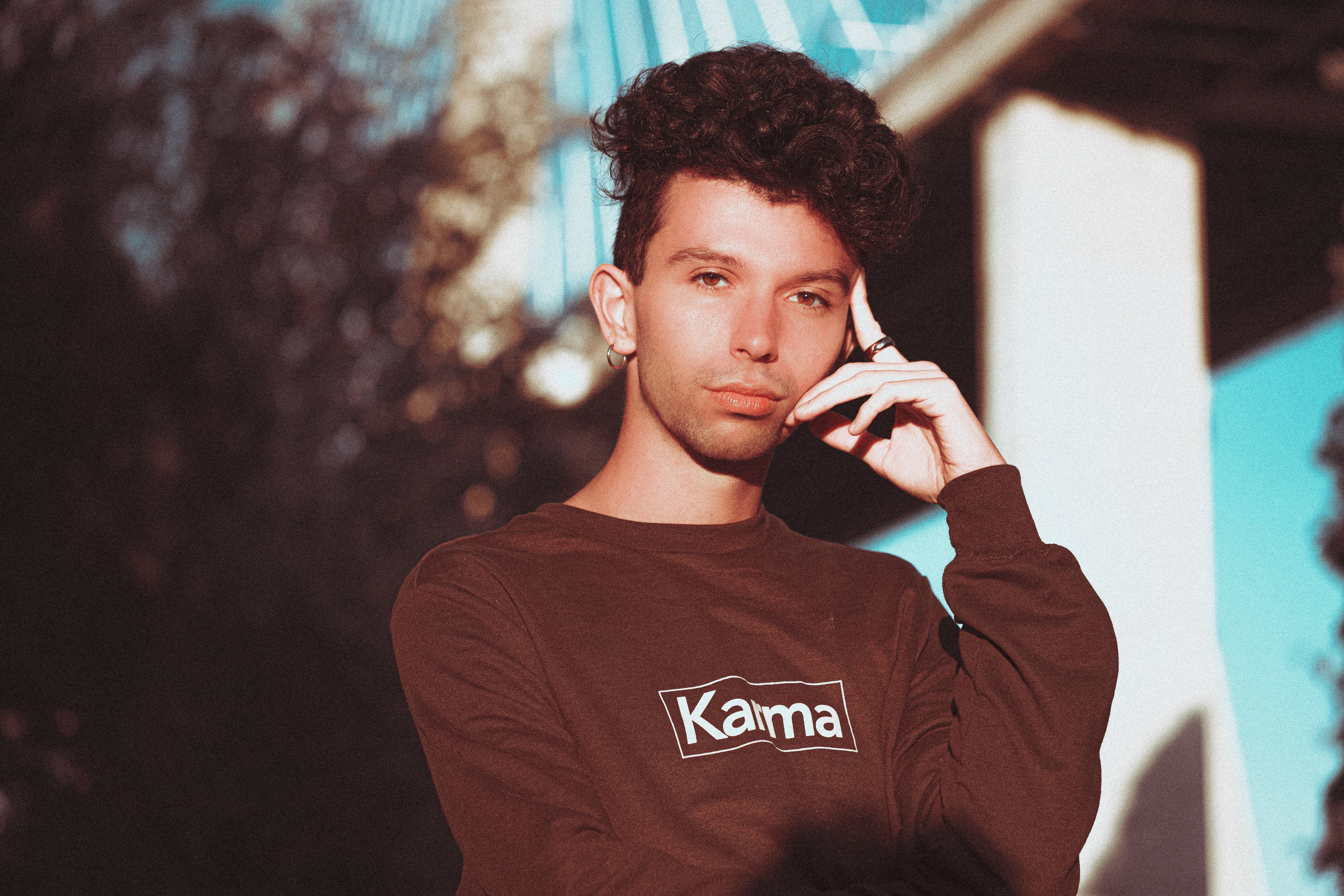 Stylish young man with curly hair posing on a sunny day, wearing a 'Karma' sweatshirt.