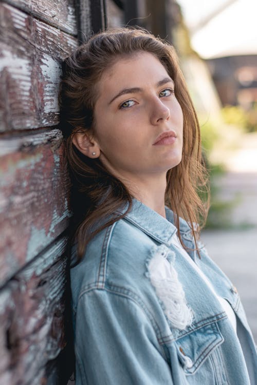 Free Woman in Blue Denim Jacket Leaning on Wooden Wall Stock Photo