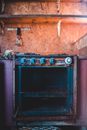Old broken metal gas stove with rusty parts placed in old kitchen under wooden shelves