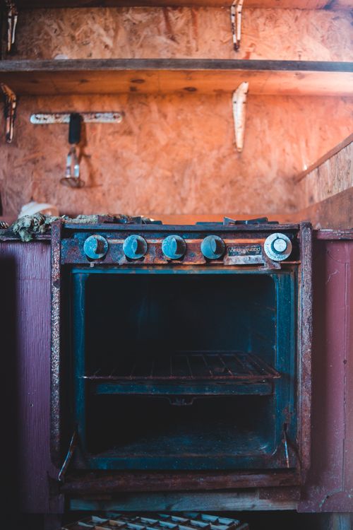 Free Old broken metal gas stove with rusty parts placed in old kitchen under wooden shelves Stock Photo