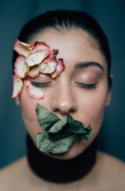 Artistic portrait of a woman with eyes closed adorned with dried petals and leaves on her face.
