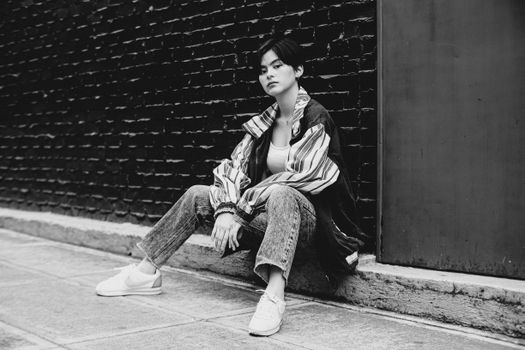 Black and white of Asian female wearing trendy shirt with jeans and looking at camera