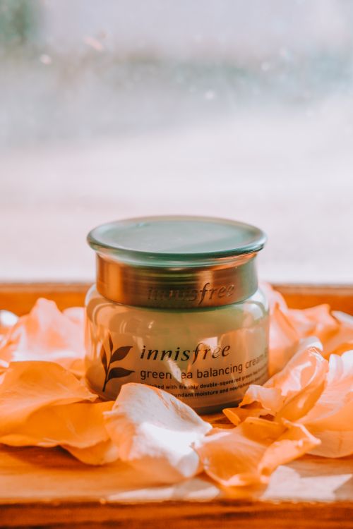 Free Innisfree Green Tea Balancing Cream jar on petals for elegant skincare. Stock Photo