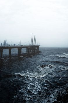 海上吊桥旁，城市天际线朦胧，海浪汹涌