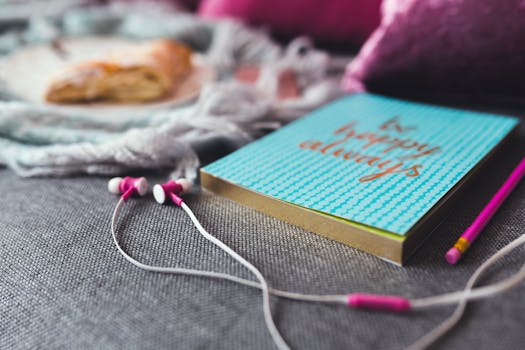 Pink earphones, a notebook with 'be happy always', and a pencil on a cozy fabric background.