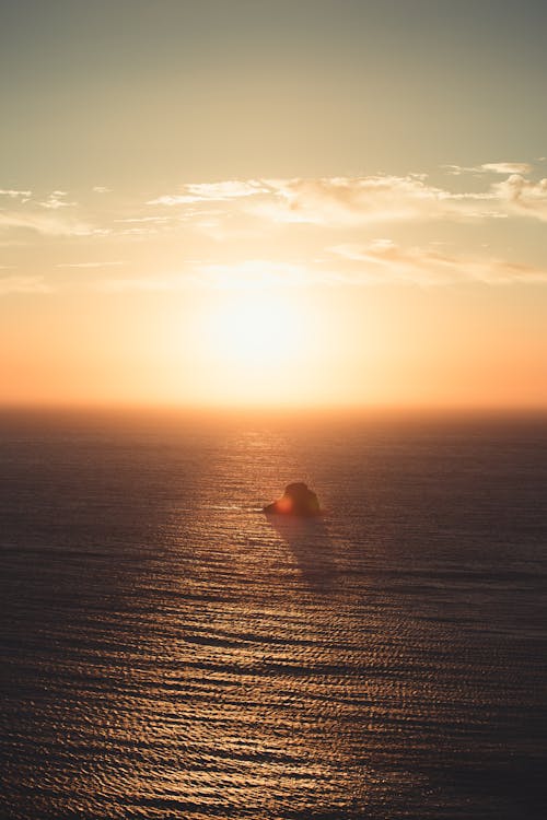 Free Shiny sun in sky above sea with rock at night Stock Photo