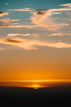 Spectacular view of colorful cloudy sky with horizon line above dark ocean at sunset