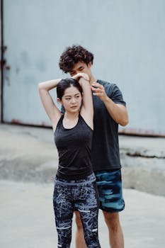 Man and woman in sportswear doing stretching exercises outdoors, guided by a trainer.