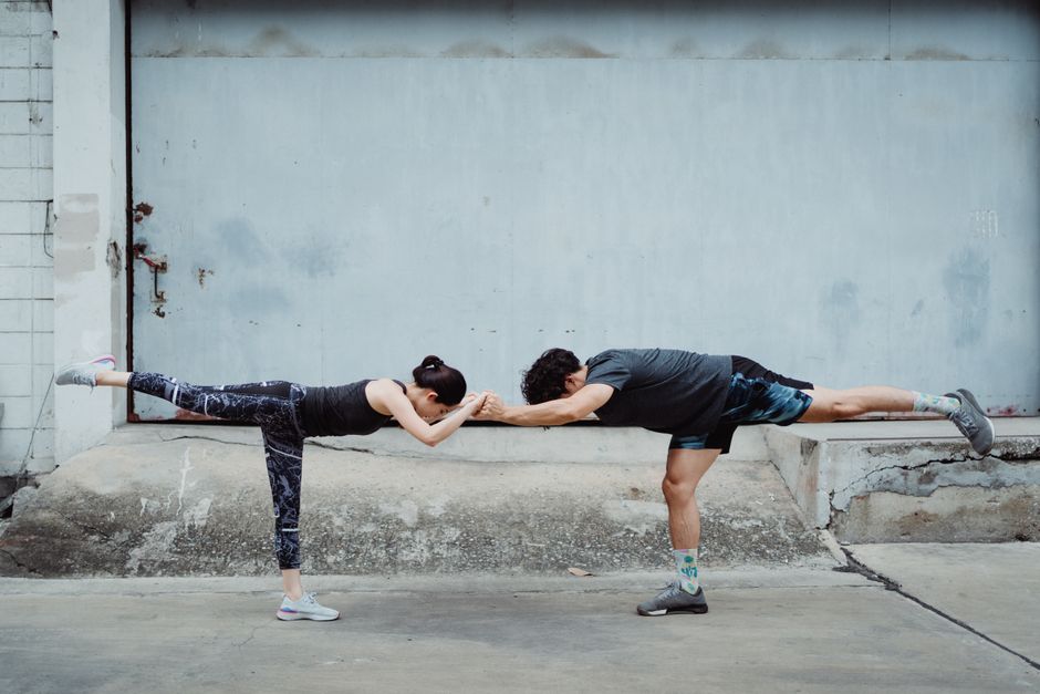 A man and woman practicing balance exercises on one leg in an urban environment.