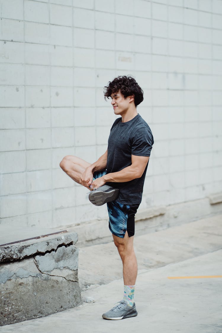 Young Man Standing On One Leg And Doing Stretching Exercise