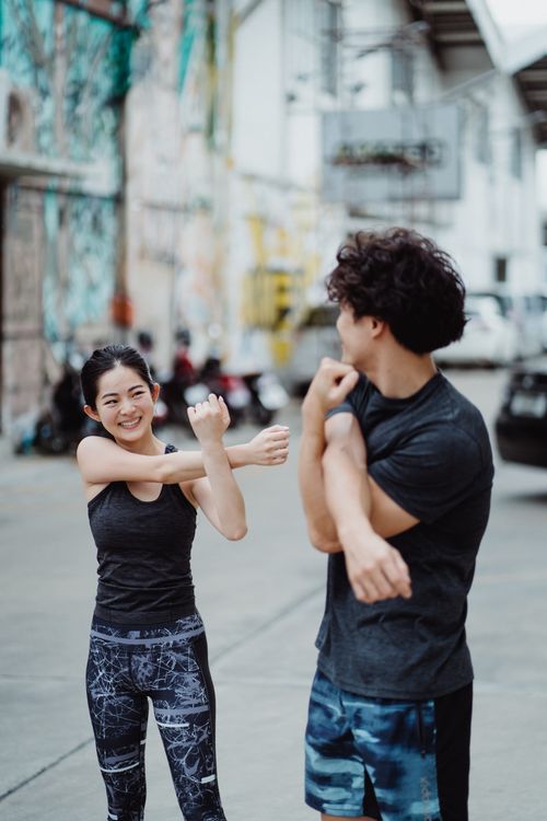 Free Smiling man and woman stretching in an urban setting before a workout session. Stock Photo