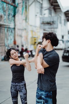 Two people in athletic wear doing stretches outdoors with urban graffiti background.