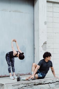A man and woman performing stretching exercises in casual sportswear outdoors.