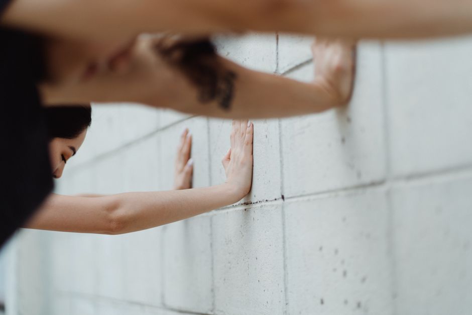 Close-up of a woman stretching with hands against a white brick wall, focusing on exercise and fitness.