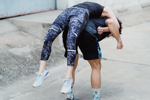 Two adults engaged in a partner workout lifting exercise outside.