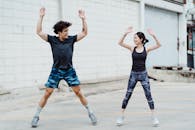 2 Women in Black Tank Top and Blue Denim Shorts Jumping on White Floor