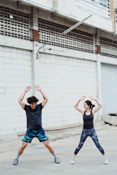 一对男女在户外建筑物旁进行跳跃表演，重点展示健身动作