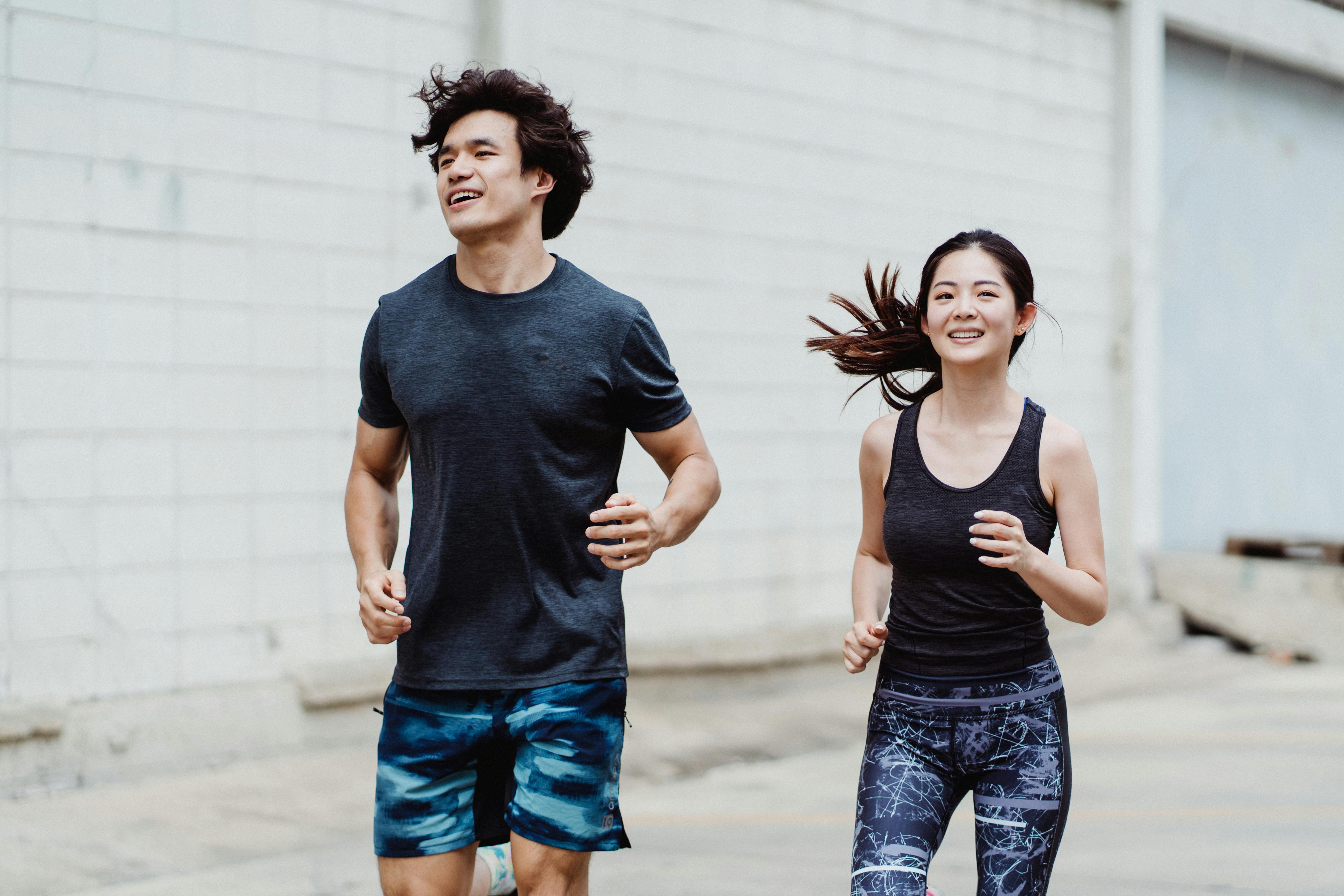 life insurance companies - A happy couple jogging together outdoors, wearing trendy activewear and smiling energetically.