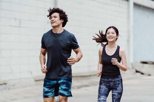 Free A happy couple jogging together outdoors, wearing trendy activewear and smiling energetically. Stock Photo